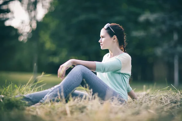 Parktaki çimlerin üzerinde oturan genç kadın.. — Stok fotoğraf