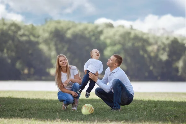 Eltern und ihr kleiner Sohn spielen mit dem Ball auf dem Rasen. — Stockfoto