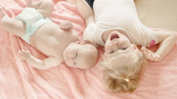 Dos hermanas pequeñas acostadas sobre una manta rosa . — Foto de Stock