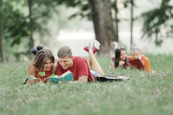 Gülümseyen bir çift öğrenci çimlerin üzerinde uzanmış kitap okuyor. — Stok fotoğraf