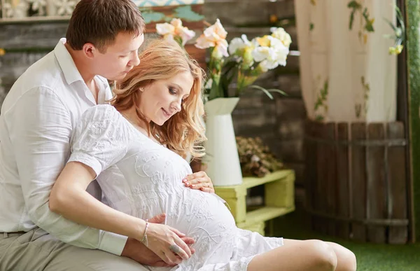 Mari étreignant sa femme enceinte assise sur le sol dans un salon confortable — Photo