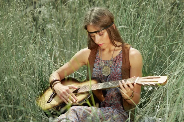 Jovem hippie mulher tocando guitarra sentado na grama — Fotografia de Stock