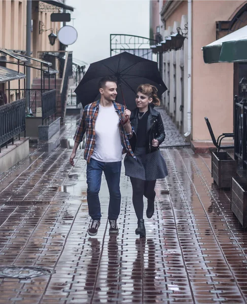Молодая влюбленная пара бежит вместе под зонтиком в дождливый день — стоковое фото