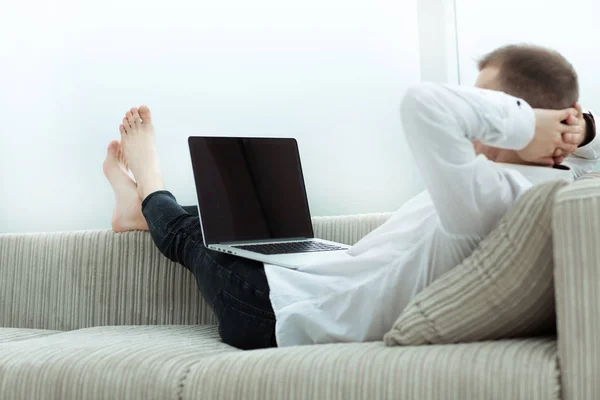 Jovem olhando para a tela do laptop enquanto deitado no sofá — Fotografia de Stock