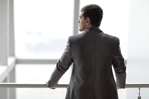 Vista trasera. hombre de negocios en ropa casual de pie y pensando cerca de la ventana de la oficina —  Fotos de Stock