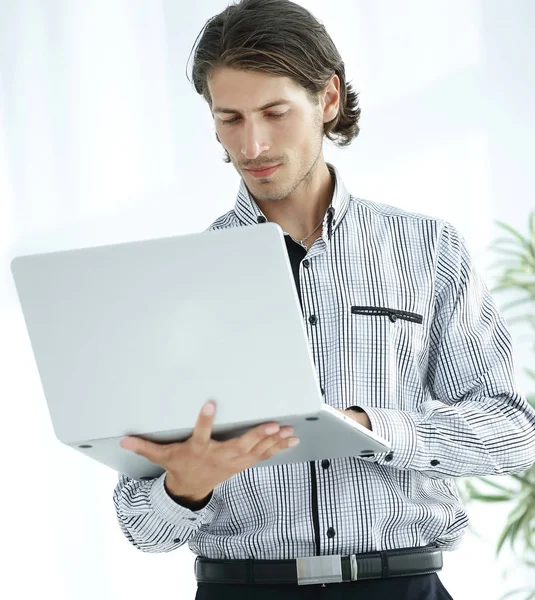 Серьезный бизнесмен, работающий на ноутбуке стоя в офисе . — стоковое фото