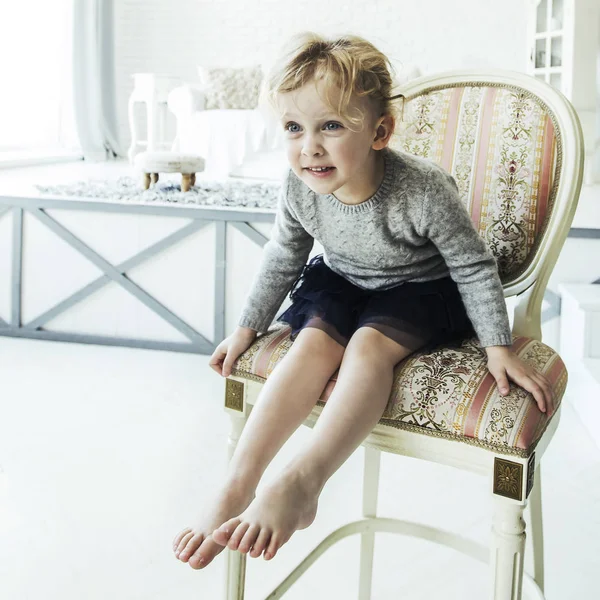 Portrait of a happy five year old girl sitting on a chair in the spacious living room — Stock Photo, Image