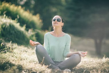 Lotus pozisyonu bulanık doğa arka plan üzerinde genç kadın.