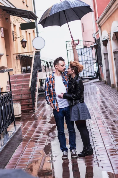 Stilig kille och hans flickvän som står under ett parasoll på en regnig dag . — Stockfoto