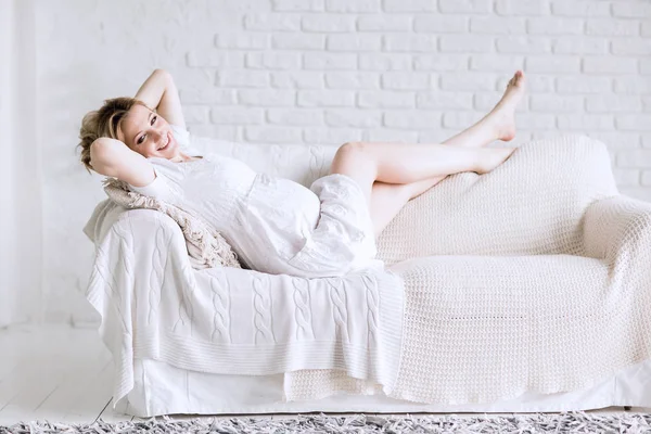 Glückliche junge schwangere Frau liegt auf Sofa im hellen Wohnzimmer — Stockfoto