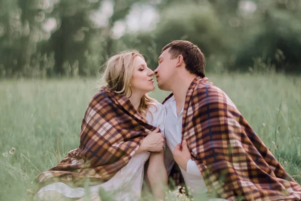 Casal, beijando sentado juntos sob um cobertor quente no gramado — Fotografia de Stock