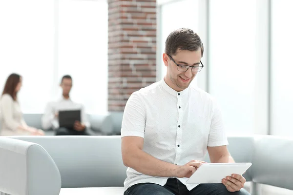 Jeune homme souriant avec tablette numérique assis dans le hall du bureau  . — Photo