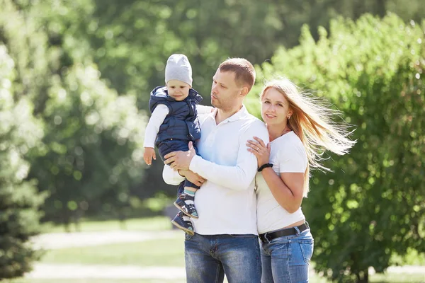 Familia feliz con un hijo pequeño en el fondo de un parque de verano . —  Fotos de Stock