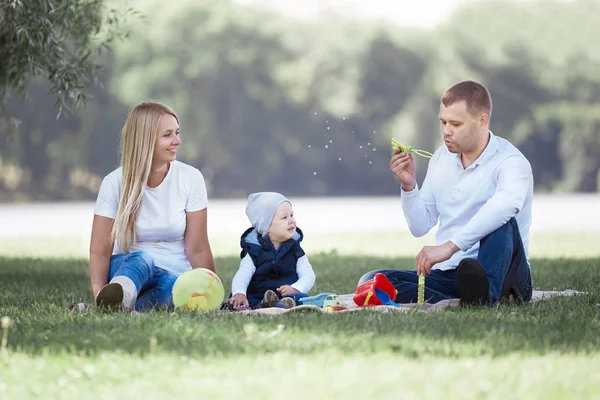 Padres y su pequeño hijo soplando burbujas en un paseo de verano . —  Fotos de Stock