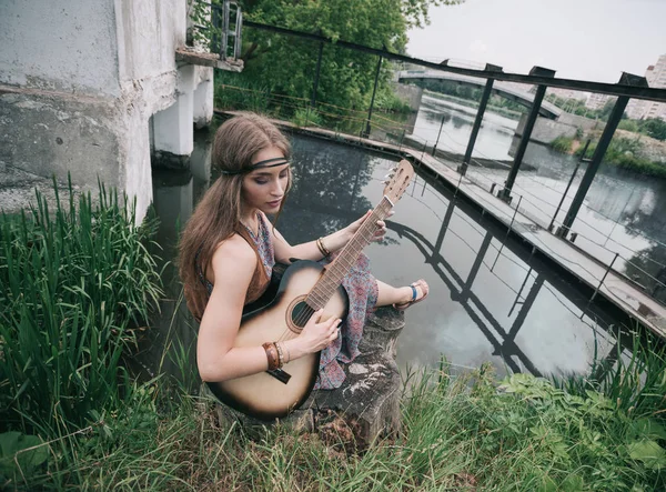 Mladí hippie žena hrající kytaru posezení poblíž rybníka — Stock fotografie