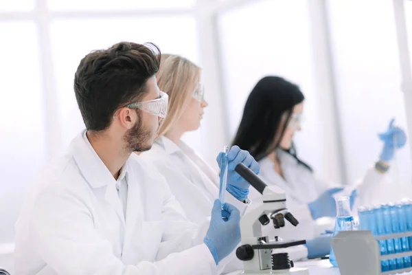 Grupo de jóvenes biólogos sentados en la mesa de laboratorio — Foto de Stock