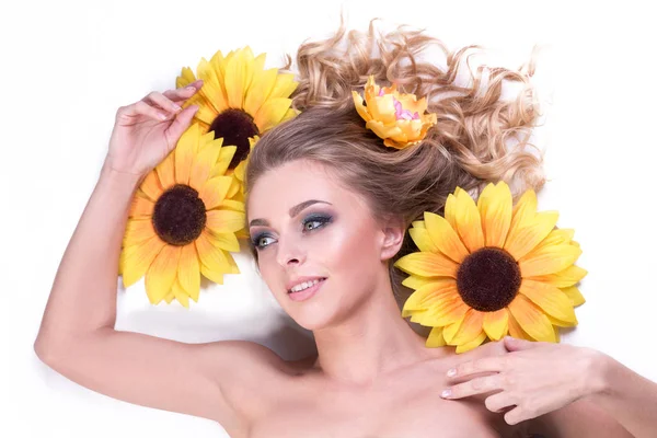 Schöne junge Frau, die zwischen den Blumen einer Sonnenblume liegt — Stockfoto