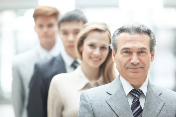 Empresário em pé na frente de sua equipe de negócios em fundo escritório turvo — Fotografia de Stock