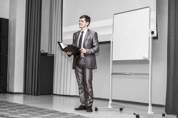 Orador detém uma apresentação de um novo projeto financeiro, de pé na frente de um conselho de publicidade em branco na sala de conferências moderna — Fotografia de Stock