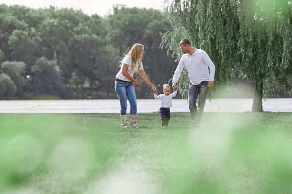 Padres felices con su pequeño hijo caminando juntos en el parque de primavera —  Fotos de Stock