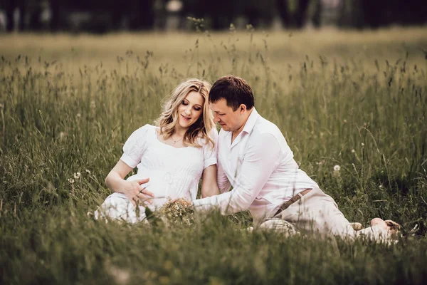 Schöne schwangere Frau mit ihrem Mann sitzt an einem Sommertag auf dem Rasen. — Stockfoto