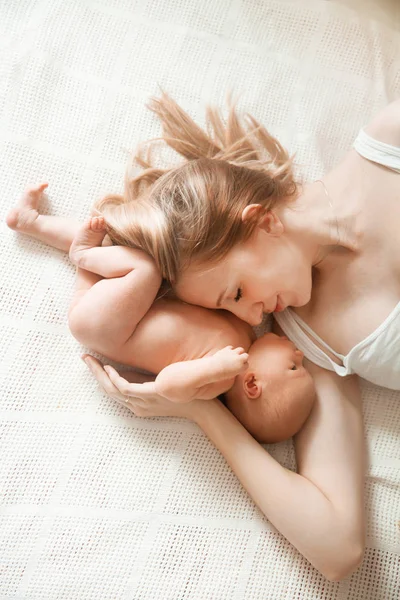 Happy mom hugs her newborn daughter lying on the bed . — Stock Photo, Image