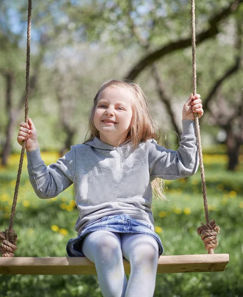 Usmívající se holčička seděla na houpačce v zahradě — Stock fotografie