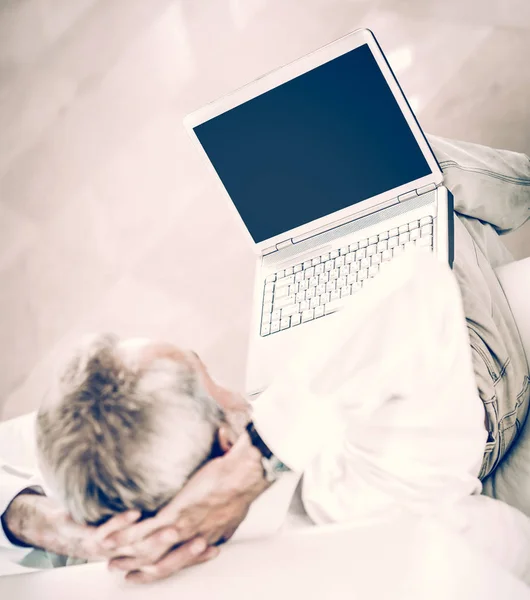 Homem de negócios visão traseira com um laptop aberto sentado no sofá no escritório moderno . — Fotografia de Stock