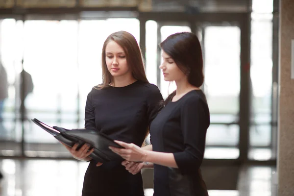 Two business women read business documents standing in the office lobby. — Stock Photo, Image