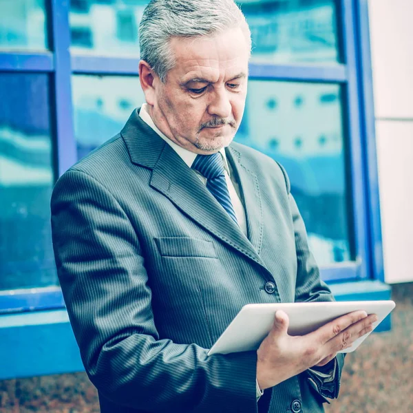 Erfolgreicher Geschäftsmann mit digitalem Tablet vor dem Hintergrund von Bürogebäuden — Stockfoto