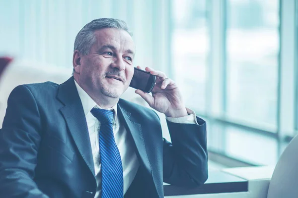 Exitoso hombre de negocios hablando en su teléfono inteligente sentado en el sofá en la oficina — Foto de Stock