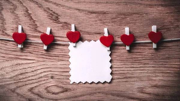 Hearts and blank note on the clothespin on wooden background. — Stock Photo, Image