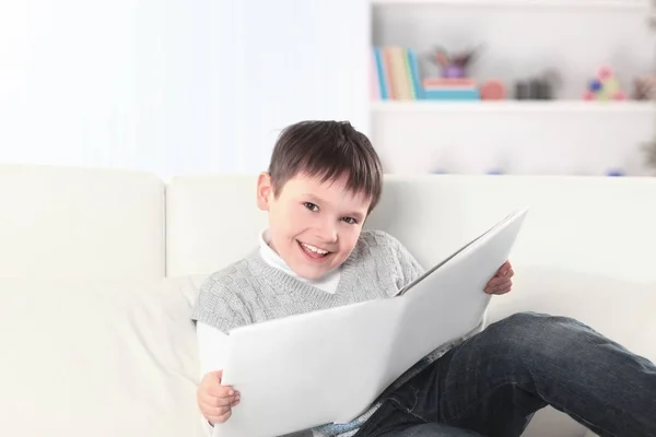 Preescolar leyendo un libro en el sofá de la guardería —  Fotos de Stock