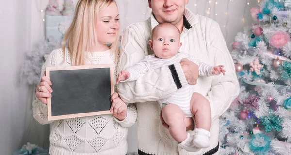 Familia feliz con una tarjeta en blanco mientras está de pie cerca del árbol de Navidad — Foto de Stock