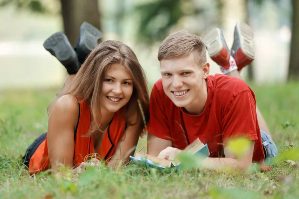 Casal de estudantes deitados na grama no Parque e lendo um livro — Fotografia de Stock