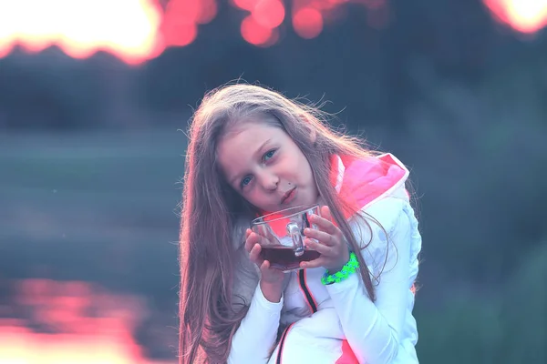 Linda niña con una taza de té sentado en un banco en el coo — Foto de Stock