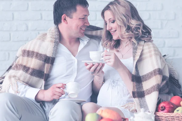 Retrato de una hermosa pareja joven, embarazada desayunando en casa después de haber cubierto a cuadros — Foto de Stock