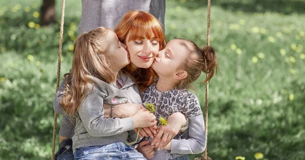 two sisters with mom swinging on a swing.