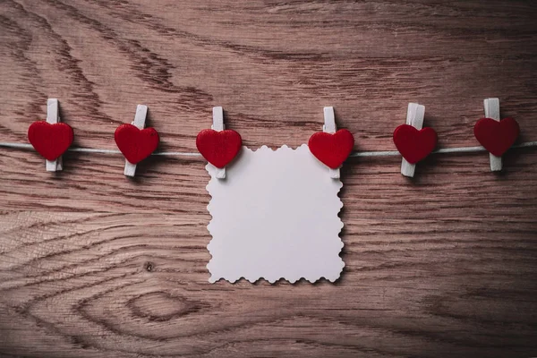 Hearts and blank note on the clothespin on wooden background. — Stock Photo, Image