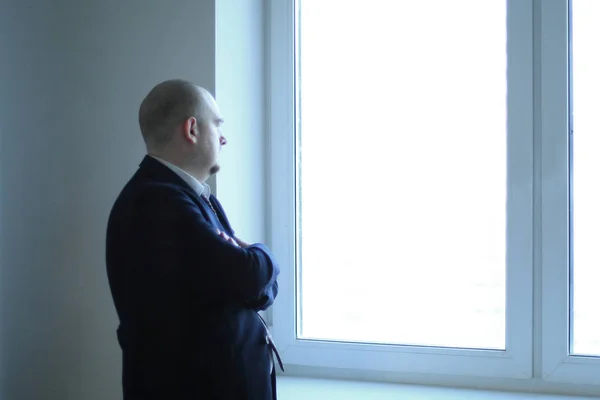 Pensativo hombre de negocios mirando una ventana de oficina en blanco —  Fotos de Stock