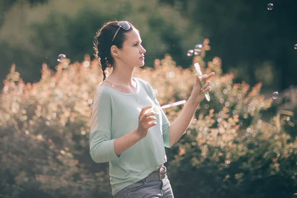 Attractive young woman playing with soap bubbles in summer Park — Stock Photo, Image