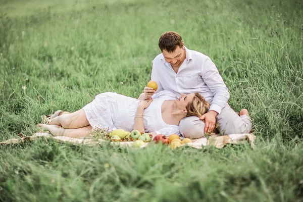 Homem feliz com sua esposa grávida descansando no gramado em um dia de verão — Fotografia de Stock