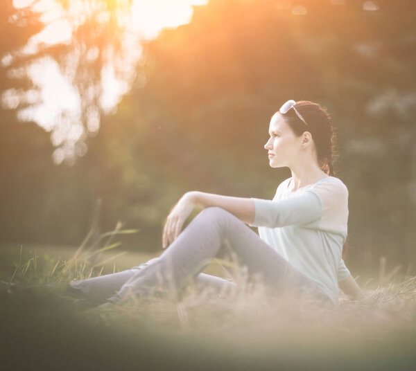 молодая женщина сидит на траве в парке.