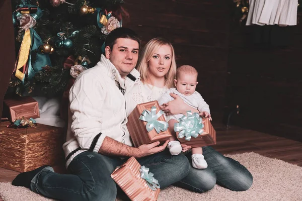 Familia feliz con cajas de regalo sentadas cerca del árbol de Navidad en Nochebuena — Foto de Stock