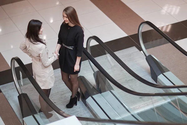 Two businesswomen talking, standing on the escalator in the business center — Stock Photo, Image