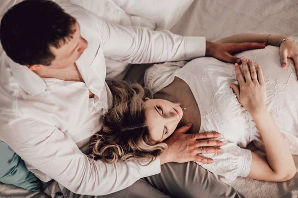 Mann umarmt seine schwangere Frau, während er auf dem Bett sitzt. — Stockfoto
