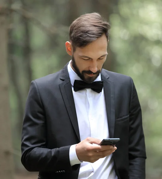 Uomo d'affari che legge SMS su smartphone in piedi nel bosco — Foto Stock