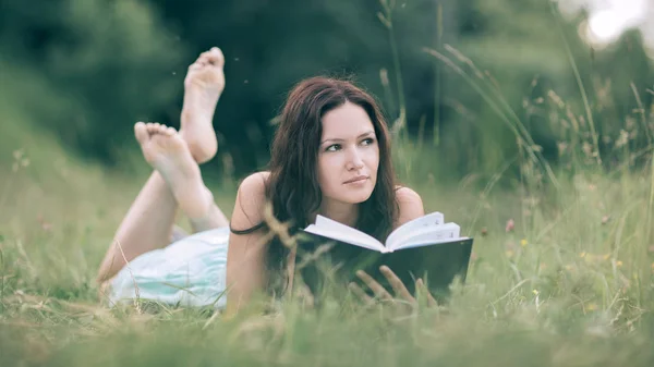 Urocza młoda kobieta czytając książkę leżącą na trawniku — Zdjęcie stockowe
