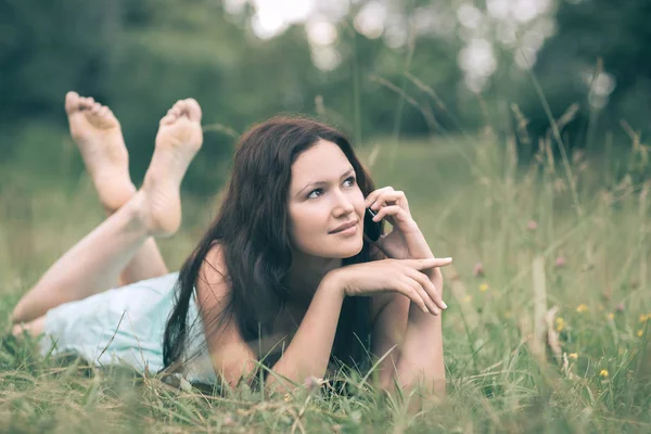 Atraktivní mladá žena, která mluví na telefonu, zatímco v létě leží na trávě. lidé a technika — Stock fotografie