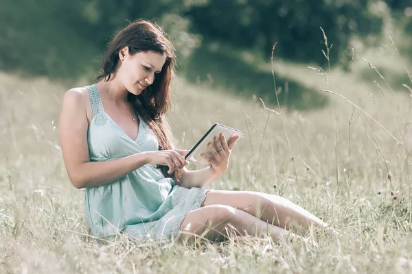 Linda chica con tableta digital sentado en el césped en un día de verano —  Fotos de Stock